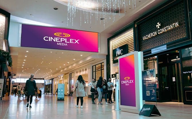 Digital screens in a shopping mall displaying Cineplex Media branding on a purple and orange gradient background