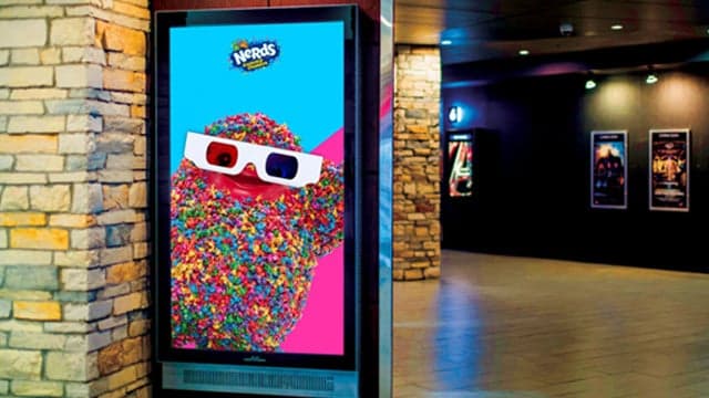 Digital ad for Nerds candy featuring colorful character with 3D glasses in a Cineplex hallway