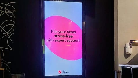 Digital screen in Cineplex hallway displaying Intuit TurboTax ad with message about stress-free tax filing