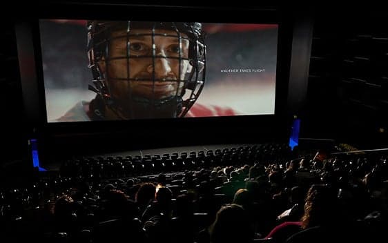 Audience watching a close-up of a hockey player on a large Cineplex theatre screen