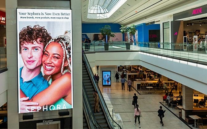 Large digital screen in shopping mall displaying Sephora advertisement with two smiling models and text about more brands and products