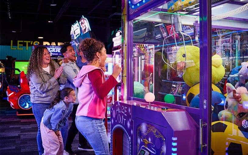 Family playing a claw machine game trying to win a large stuffed toy at an arcade