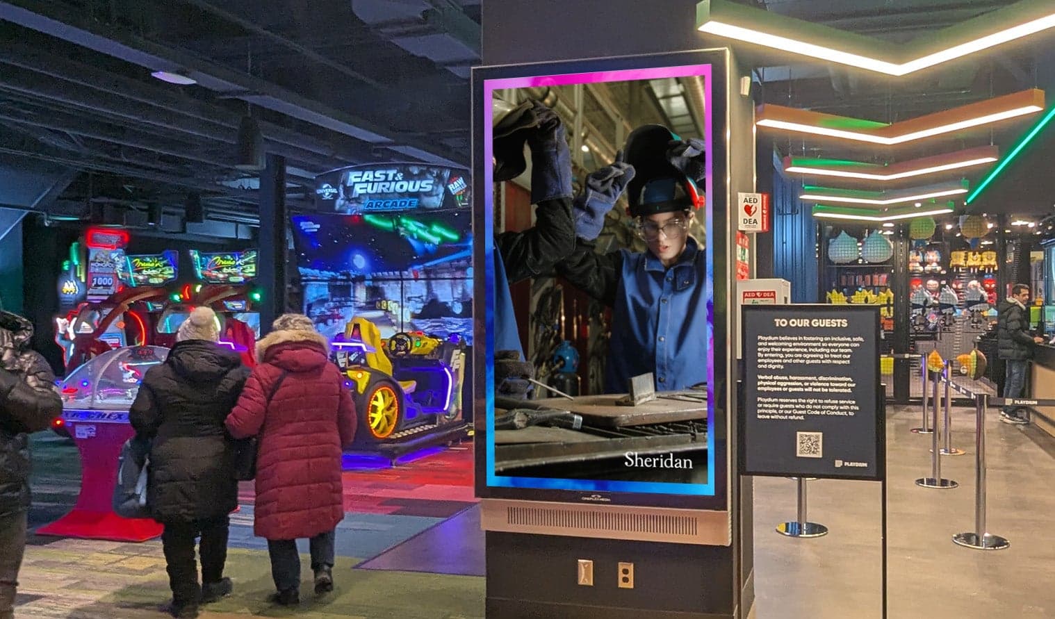 Digital screen at Playdium Brampton displaying Sheridan College advertisement near the arcade area