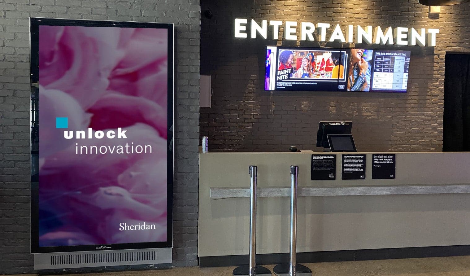 Digital screen at The Rec Room Square One featuring Sheridan College ad with the text “unlock innovation”