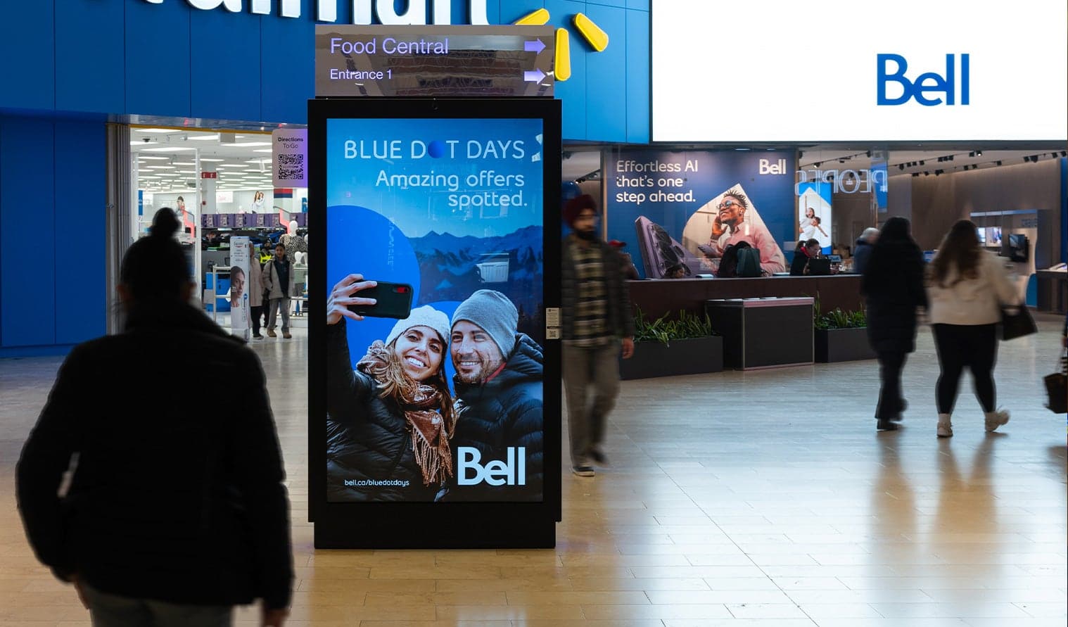 Shoppers walking past a Bell digital advertisement in a mall corridor