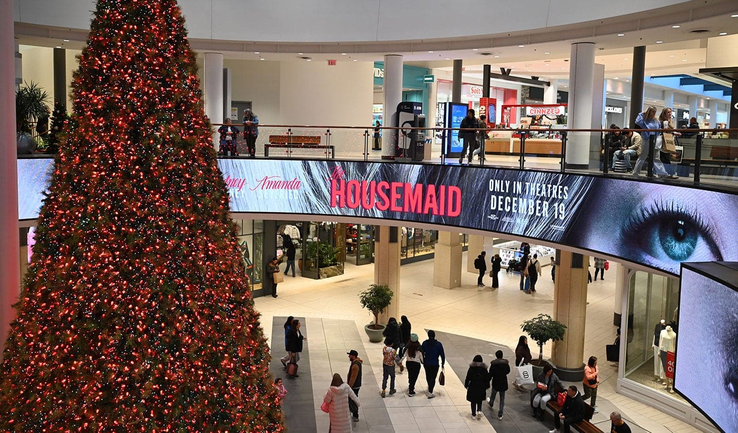 Shoppers in a decorated mall with a large Christmas tree and digital ad display