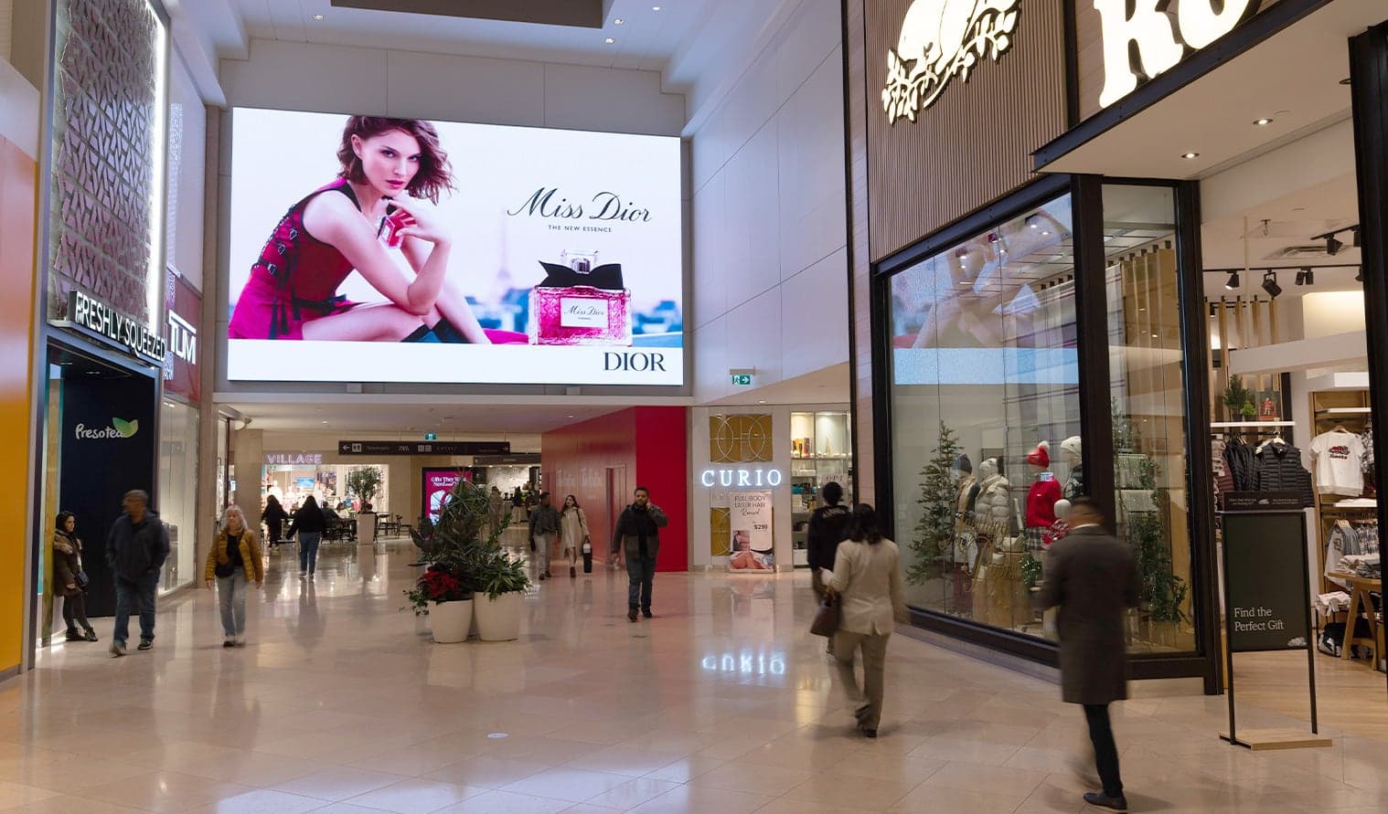 Shoppers walking in a mall corridor with a large Miss Dior digital ad display