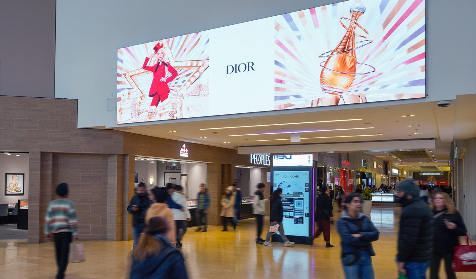 Large overhead digital display showing Dior advertisement in a busy Square One mall corridor