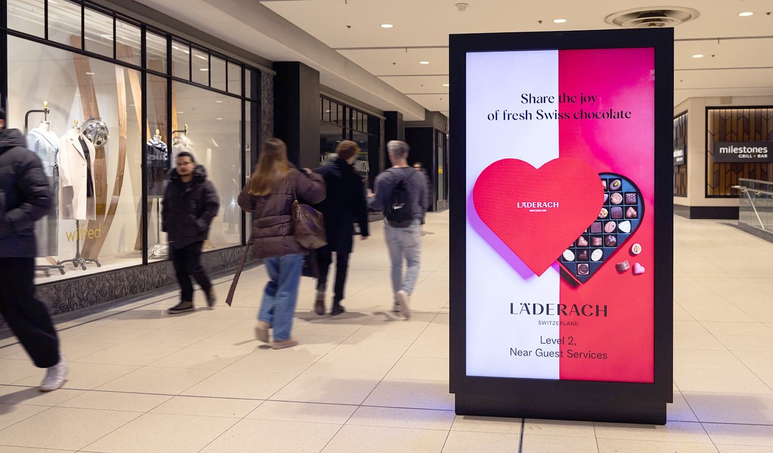 Mall shoppers walking past a digital ad for Läderach chocolates featuring a heart design at CF Toronto Eaton Centre