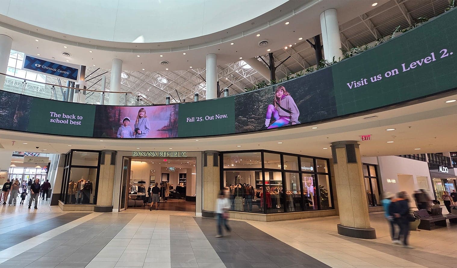 Curved digital display promoting Roots store above main entrance at CF Chinook Centre