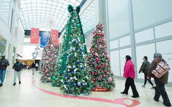Shoppers walking past Starbucks-branded Christmas tree display in a mall holiday activation