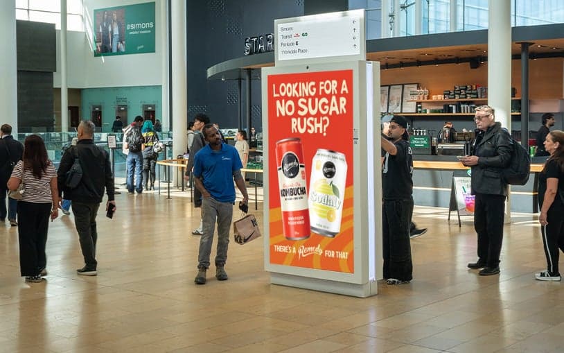 Shoppers walking past a digital ad for no-sugar beverages in a mall corridor
